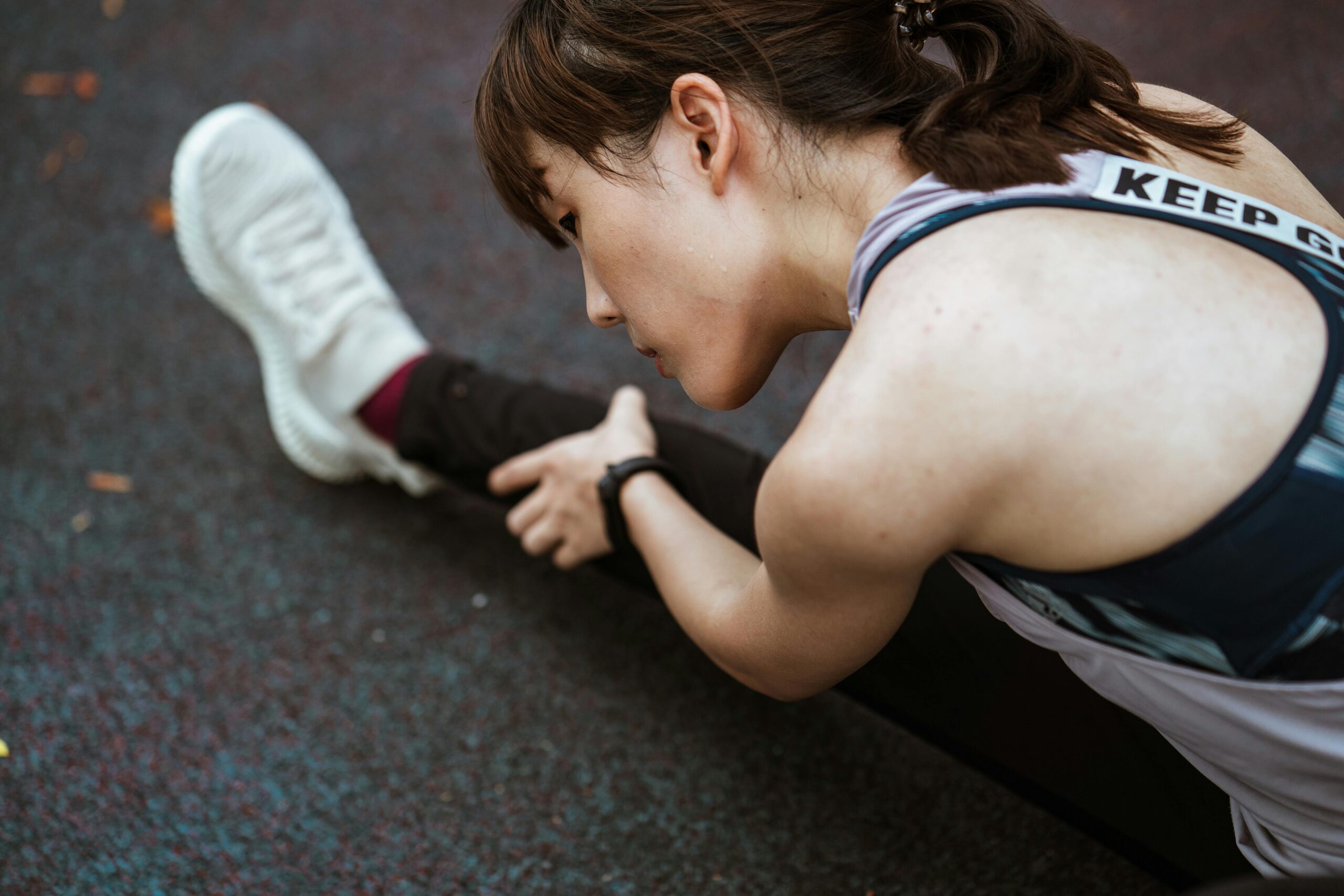 Home From above calm focused ethnic flexible female in sportswear warming up on sports ground